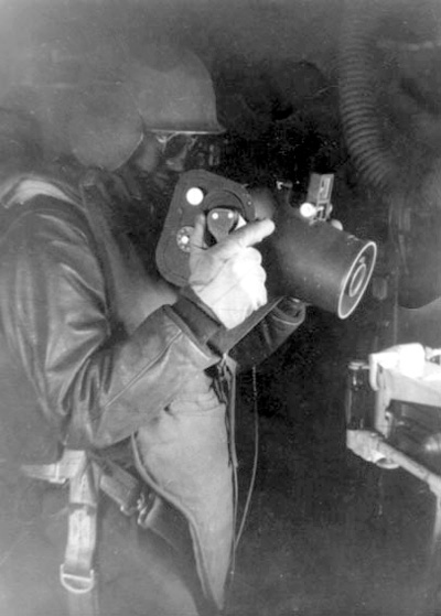 An aerial photographer with the United States Army Air Forces dressed in a flak vest and flak helmet and holding a Graflex K-20 aerial camera, based on the Fairchild design, 1943-44.