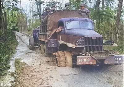 US Army 2 1/2-ton 6x6 cargo truck towing a piece of field artillery through heavy mud in the South Pacific, date unknown; bumper markings showed 98th Division, 369th Field Artillery [Colorized by WW2DB]