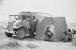 Canadian Ford-built CMP 3/4-ton 4x4 truck with Bedford-built after body serves as a windscreen for British soldiers setting up a tent in the North African desert, 1942.
