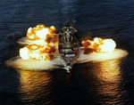 Aerial bow view of USS New Jersey firing her nine 16-inch guns simultaneously on either side of her, 30 Dec 1986