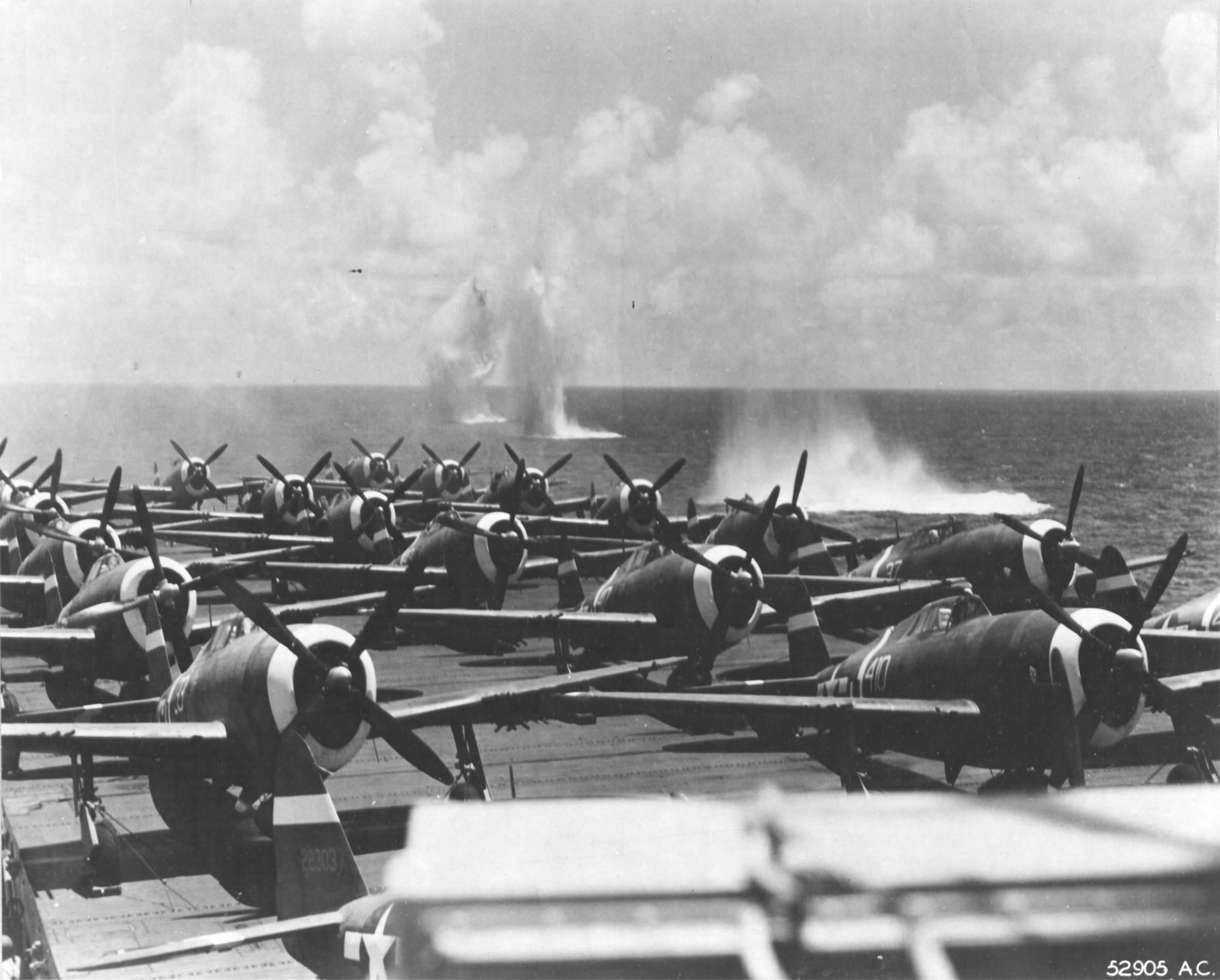 P-47D Thunderbolts of the 318th Fighter Group being ferried to Saipan on Escort Carrier USS Manila Bay. Note bomb splashes from an aerial attack by four D3A Aichi “Val” dive bombers during refueling operations east of Saipan, Jun 23 1944. Photo 1 of 2