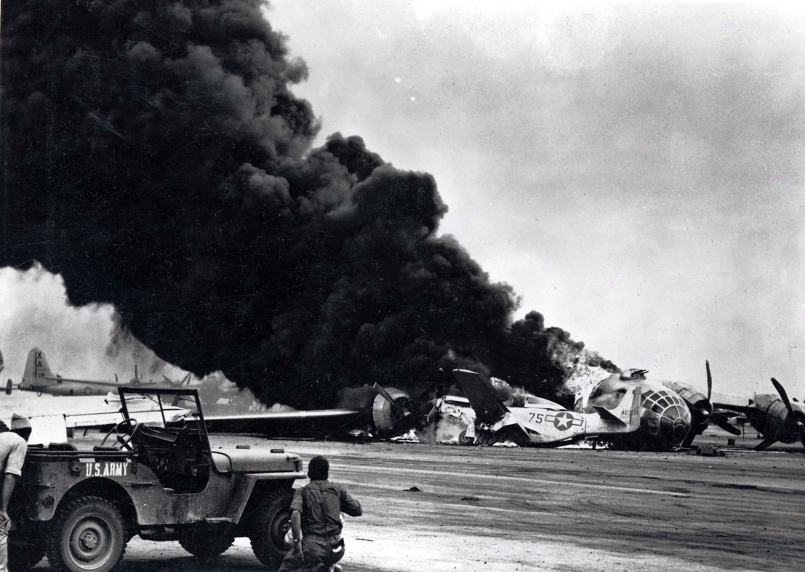 A B-29 Superfortress crashed during an attempted emergency landing on Iwo Jima Apr 24, 1945 and ran into nine P-51 Mustangs. Ground personnel wait behind a Jeep for all ammunition to cook off.