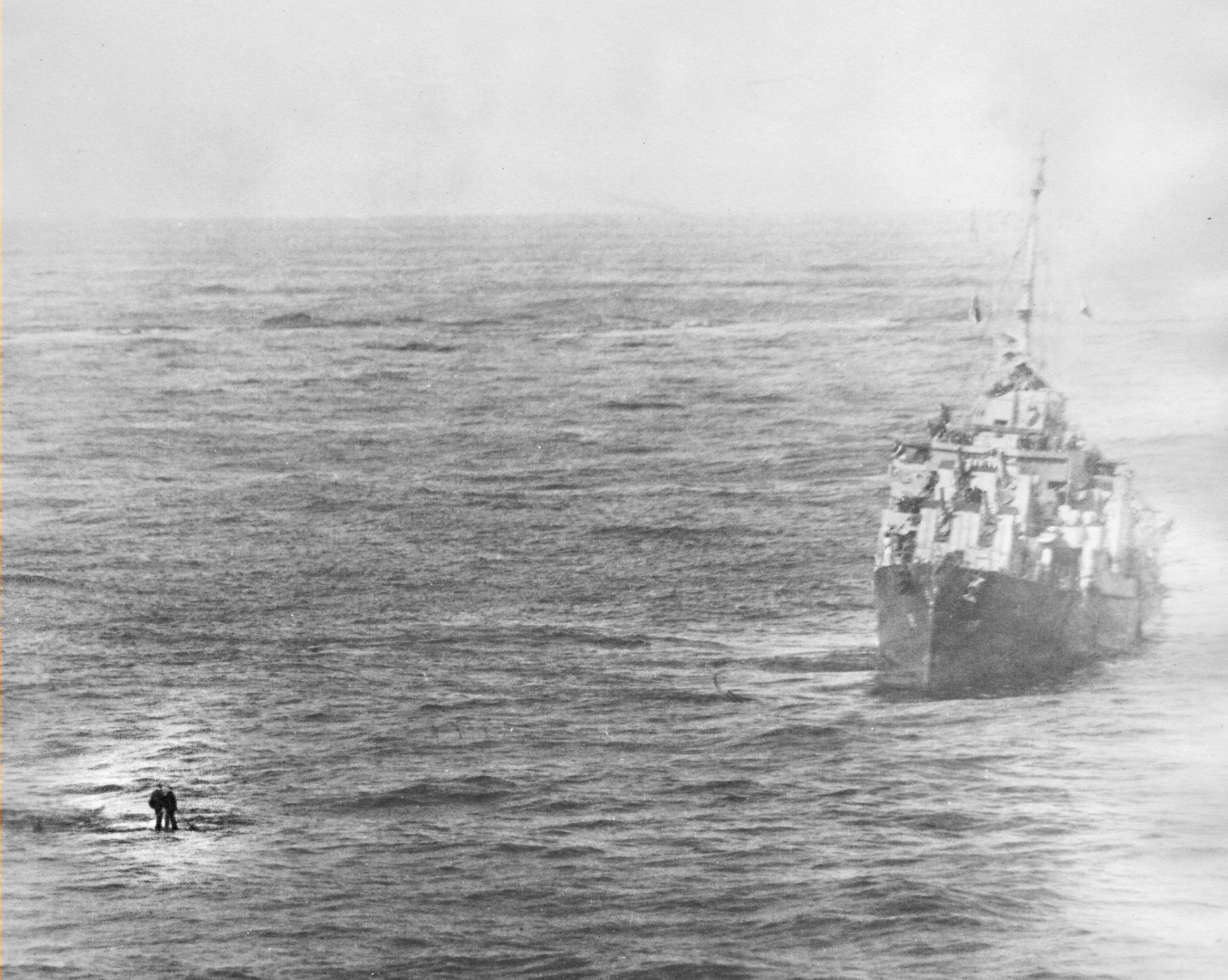 Two sailors from USS Enterprise stand on a section of the forward elevator awaiting rescue from USS Waldron after being blown into the water by the same explosion that sent the elevator high into the air, 14 May 1945.