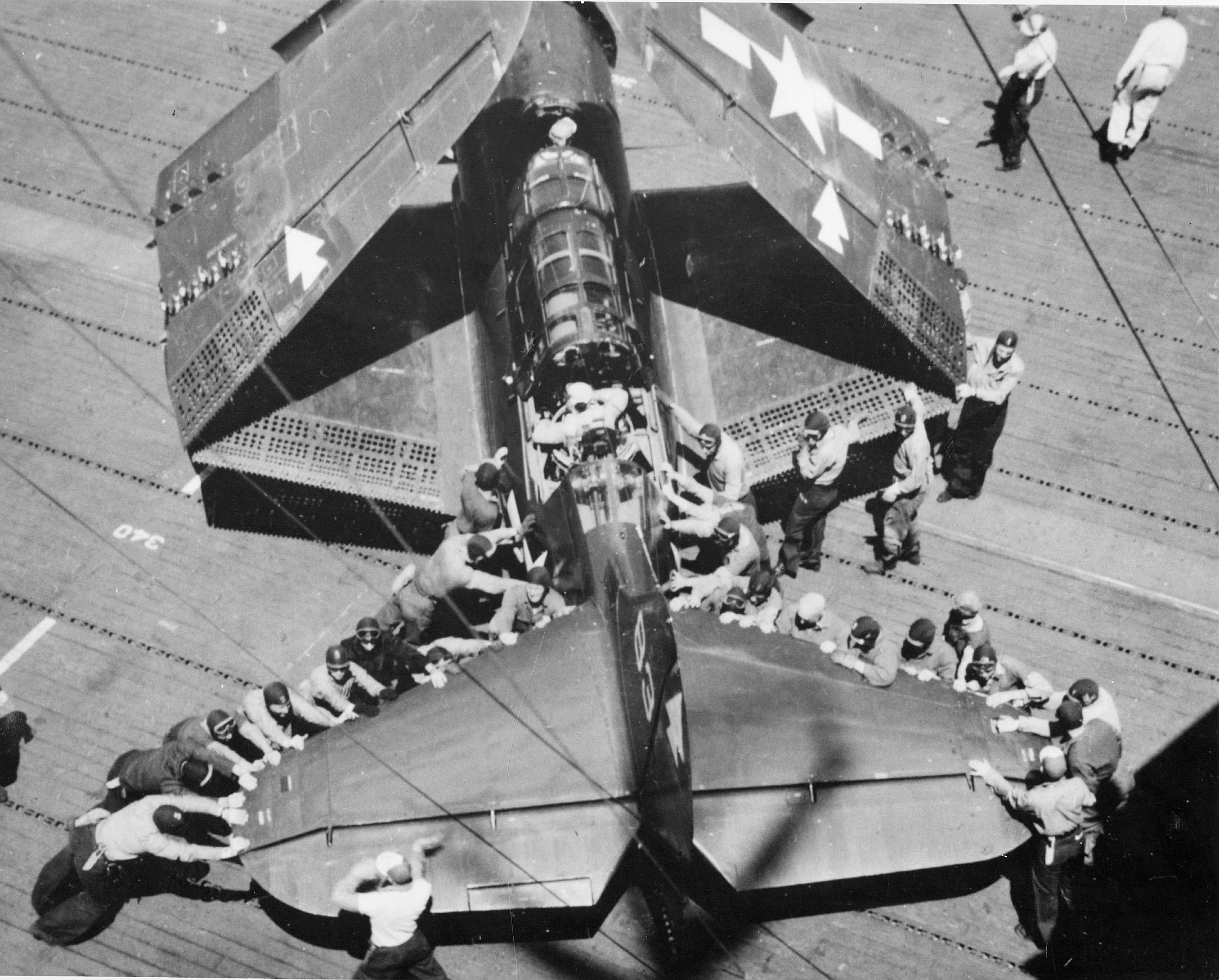 Overhead view of plane handlers spotting an SB2C Helldiver aboard USS Bennington, early 1945. This view offers a good look at the large surface area of the Helldiver’s tail plane.