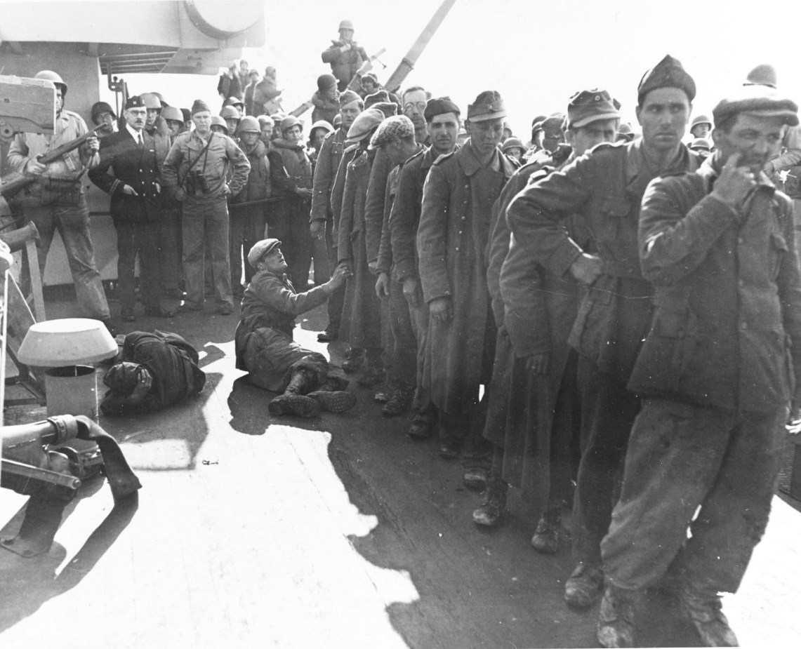 German and Italian prisoners of war from the Normandy campaign en route Britain on the battleship USS Texas, Jun 1944. Some are sitting due to seasickness. Note guard holding a Reising M50 submachinegun.
