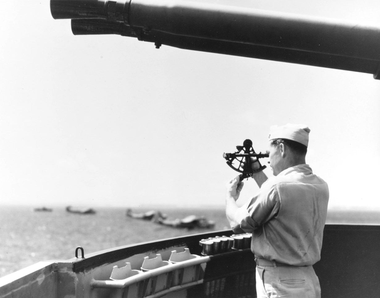 US Navy Lt Robert S Selby shoots the sun with a sextant inside one of the 40mm gun tubs aboard seaplane tender USS Castle Rock, Tanapag Harbor, Saipan, Apr 1945. Note 40mm ammunition racks and PBM Mariners beyond.
