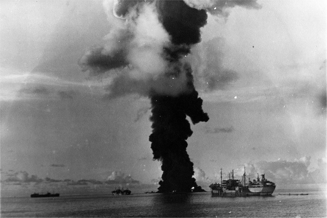 A column of smoke 500 feet wide rising from the capsized and burning fleet oiler USS Mississinewa after being struck by the first Japanese Kaiten deployed, Ulithi Atoll, 20 Nov 1944. Oiler USS Pamanset in the foreground.