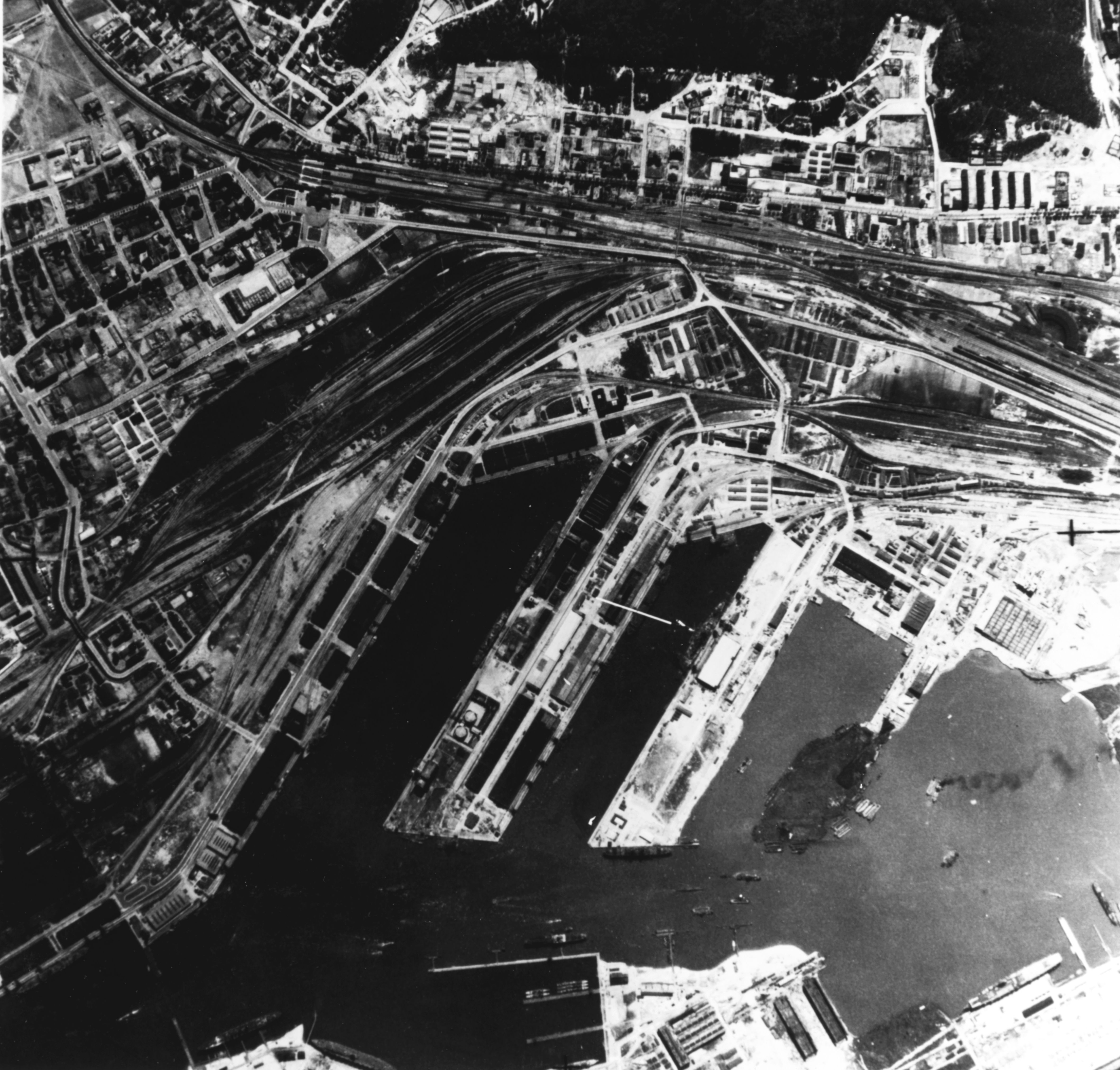 Aerial view of Gotenhafen (Gdynia), occupied Poland, Jun 1942, photo 1 of 2; photo taken by a British RAF aircraft; note battlecruiser Gneisenau (white arrow) and carrier Graf Zeppelin (bottom)