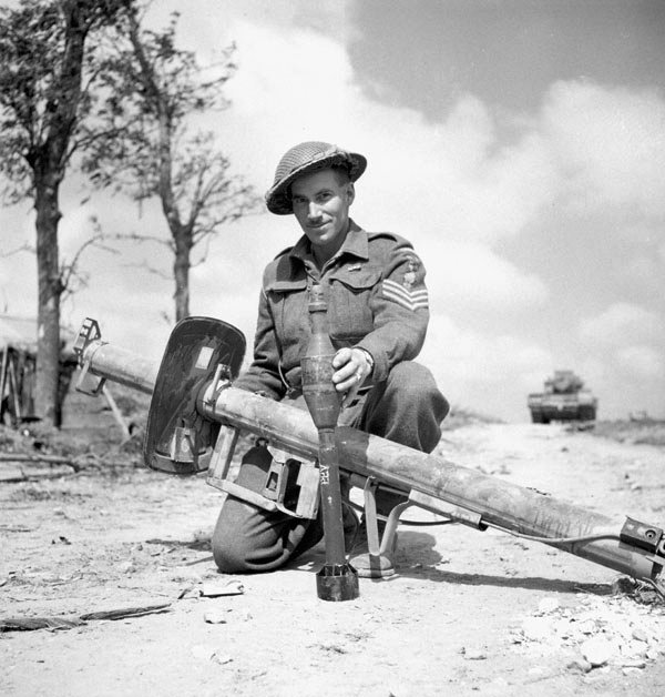 Sergeant V. R. Francis of 19th Field Regiment, Royal Canadian Artillery with a captured German Panzerschreck weapon and 88mm ammunition, France, 16 Jun 1944