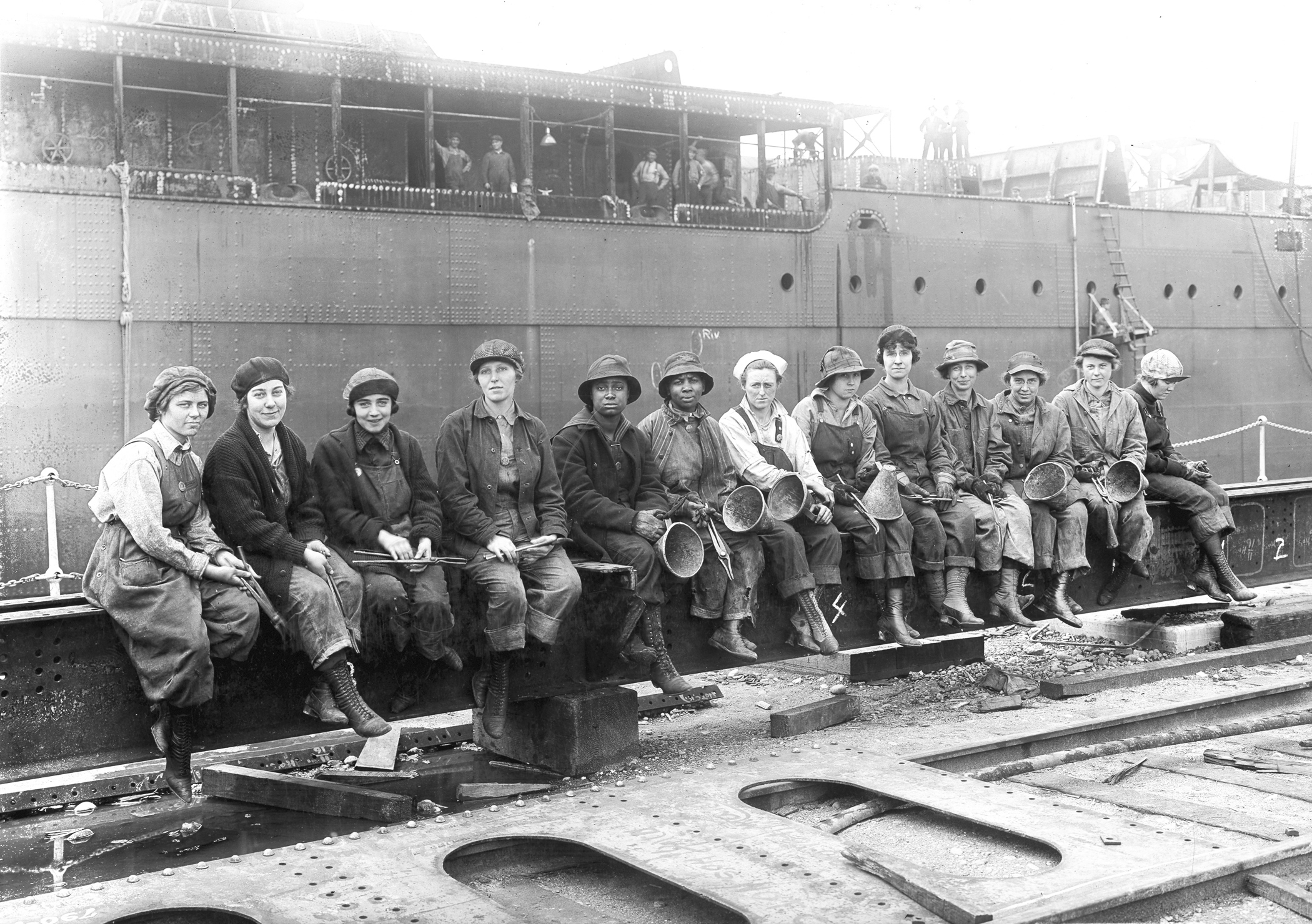 Thirteen women rivet heaters and passers at the Puget Sound Naval Shipyard, Bremerton, Washington, United States, 1919.