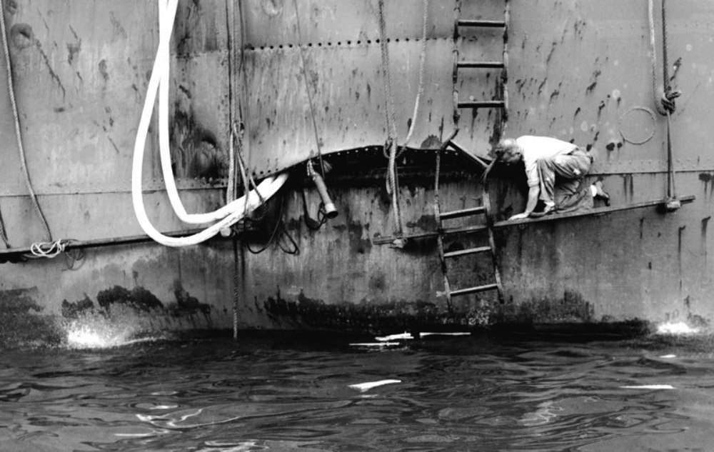 Workmen inspecting the hull damage to USS Nashville in Jun 1944 after a bomb near-miss in the Bismarck Sea on 4 Jun 1944. Photo probably taken at Seeadler Harbor, Manus Island. Note the shrapnel splatter pattern.