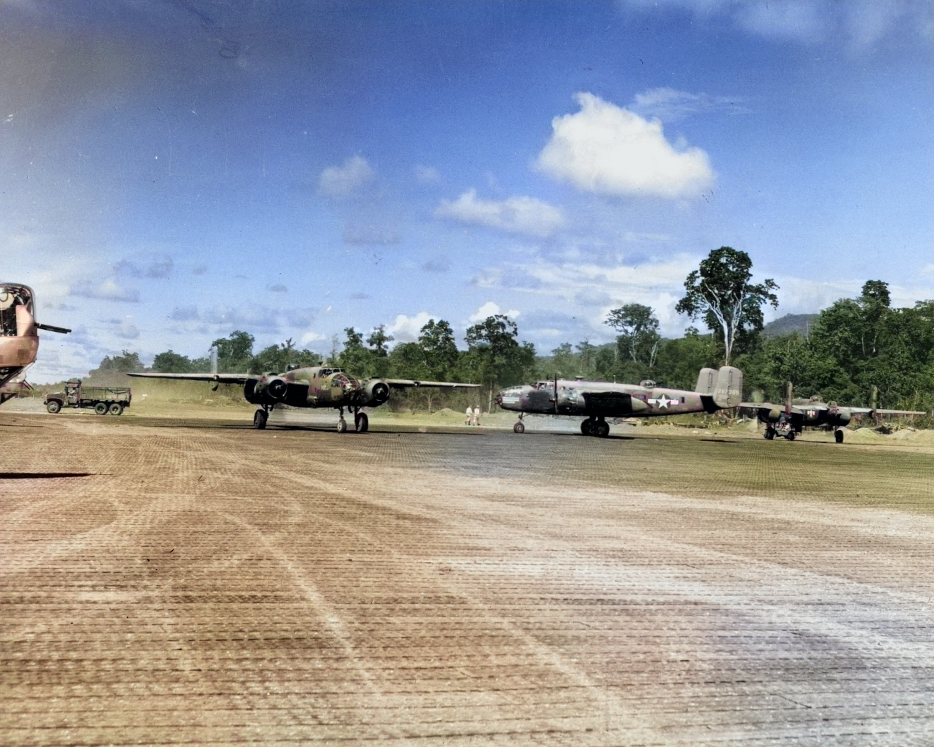 B-25 Mitchell bombers of the 42nd Bomb Group on the ramp at Munda, New Georgia, Solomons, 1943. Note B-24 Liberator nose turrets at left. [Colorized by WW2DB]