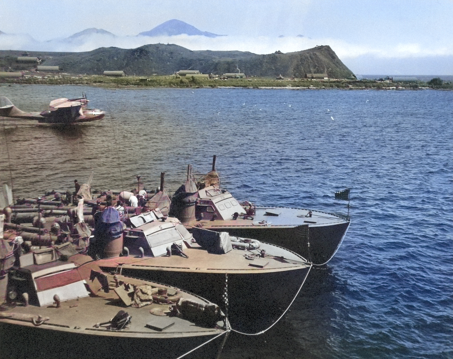 Higgins 78-foot torpedo boats of Motor Torpedo Boat Squadron 13 (MTBRon 13) moored in Attu, Alaska, Jul 943. Note PT-75 and PT-78 nested outboard of their squadron-mate and PBY Catalina patrol plane taking off. [Colorized by WW2DB]
