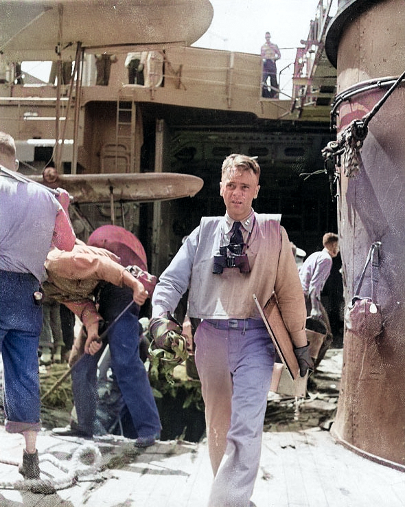 US Navy pilot Lt Wilson R. Bartlett of cruiser Chester returning from observation flight to Taroa, Marshall Islands, 1 Feb 1942; note bomb damage in background and wingtips of his SOC Seagull aircraft [Colorized by WW2DB]