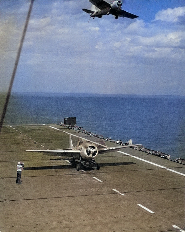 A FM-2 Wildcat fighter prepared to launch from USS Charger while another flew overhead, Chesapeake Bay, Maryland, United States, 8 May 1944 [Colorized by WW2DB]