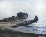 Supermarine Spitfire of the US 307th Fighter Squadron rests on the beach at Paestum, Italy near Salerno after being shot down Sep 9, 1943; pilot uninjured. LST-391 unloads men and materiel beyond, Sep 1943. Photo 1 of 2