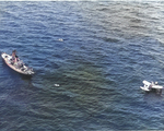 OS2U Kingfisher floats on the ocean near a US Coast Guard cutter as they rescue survivors of a merchant ship torpedoed off the US East Coast; photograph from a US Navy airship, 1942