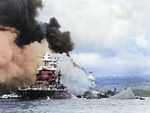 A bow-on view of the comparatively lightly damaged battleship USS Maryland with the burning USS West Virginia behind her and the capsized USS Oklahoma beside her, Pearl Harbor, US Territory of Hawaii, 7 Dec 1941