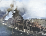 USS Franklin burning and listing after being hit by a Japanese bomb off Japan, 19 Mar 1945. Note firefighting water pouring off the hangar deck into the sea. Photo taken from USS Santa Fe.