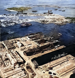 Aerial view of shipping in the Pearl Harbor Navy Yard repair basin with Ford Island beyond, 12 Dec 1943. Note the camouflage patterns painted on the roofs of the buildings.