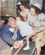 American Private First Class Lee Harper, wounded at Normandy, was greeted by his 2-year-old sister Janet, whom he had never seen before, as his mother and wife looked on, New York City, 1 Aug 1945