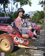 US Army Corporal Paul F. Janesk posing in his jeep in Sicily, Italy, 3 Sep 1943; note cartoon of Axis leaders drawn on his jeep, and Mussolini crossed out