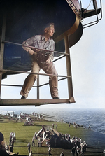 LtCdr Edward Steichen with his camera on an island catwalk above the flight deck of the USS Lexington (Essex-class), Nov 1943, probably off Hawaii. Note F6F Hellcats on the flight deck.