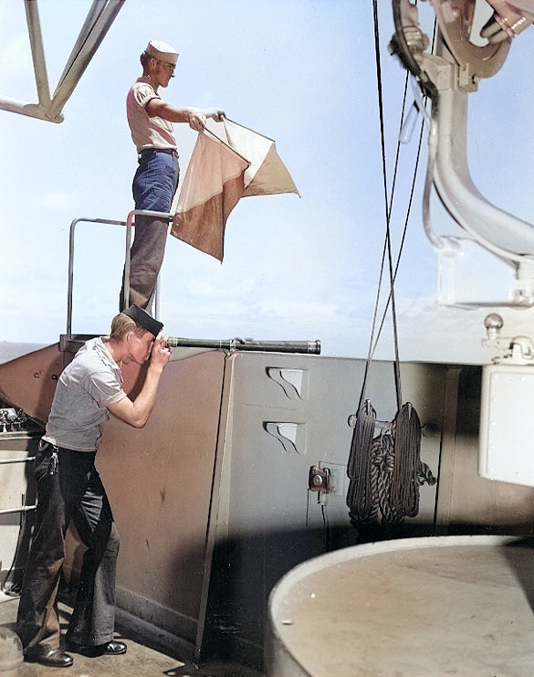 US Navy Signalman 2nd Class Kenneth Mitchell of battleship Colorado sending a message with semaphore flags, 29 Oct 1943; Signalman 3rd Class John Wilson on telescope [Colorized by WW2DB]