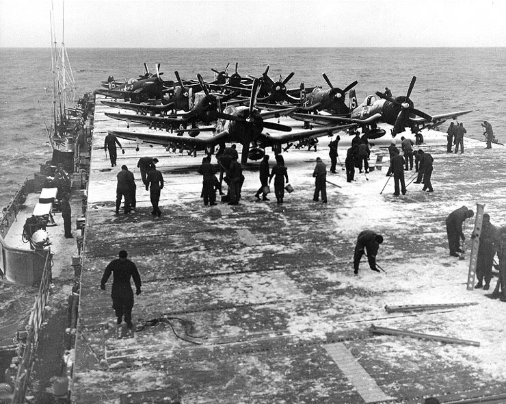 Crewmen of USS Badoeng Strait clearing snow from the flight deck, off Korea, 14 Nov 1950; note F4U-4B fighters of US Marine Corps squadron VMF-323