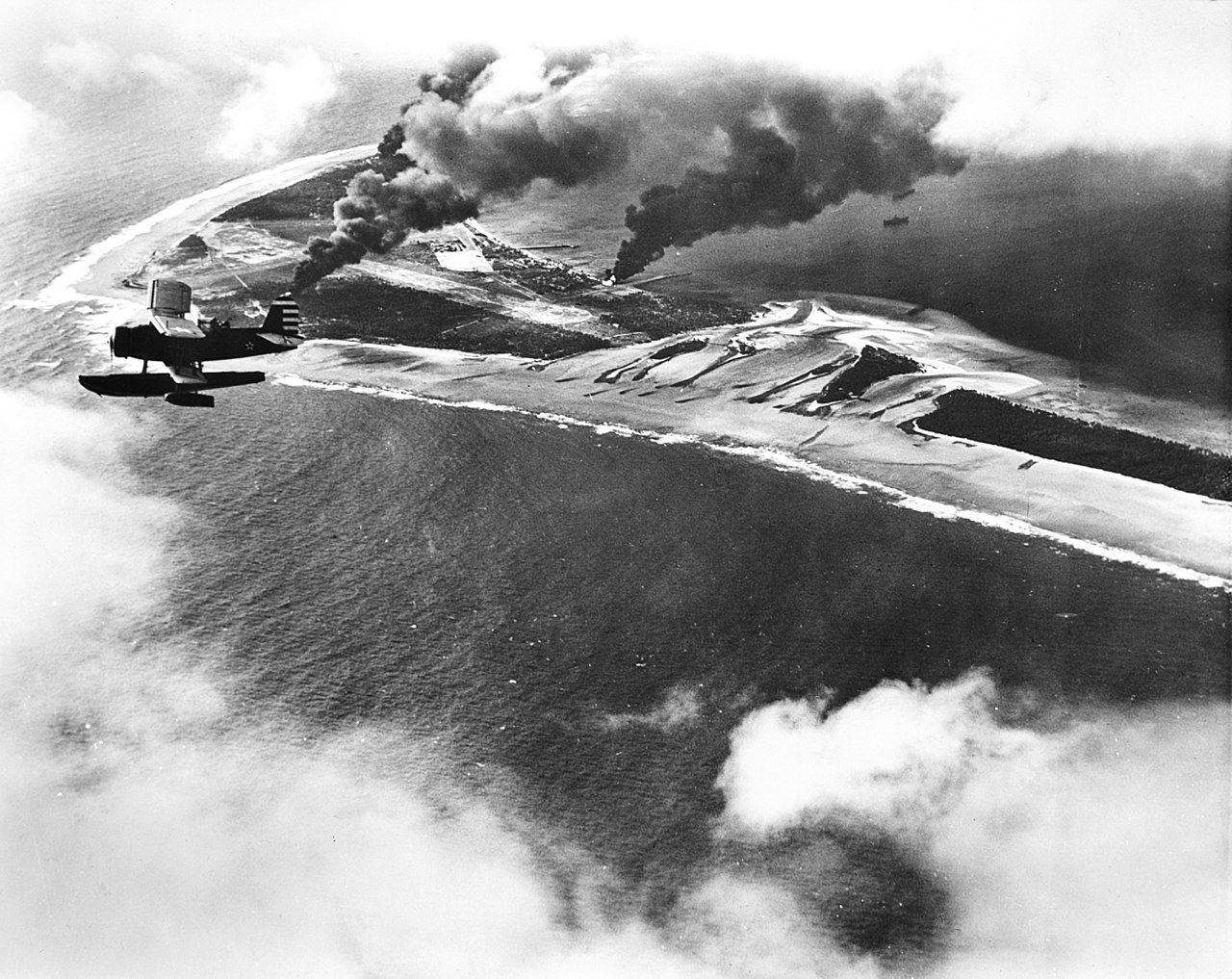 SOC aircraft flew over Wotje Atoll, Marshall Islands, during attack on Japanese airfields by gunfire from cruisers Salt Lake City and Northampton, 1 Feb 1942; note burning ammunition and fuel dumps