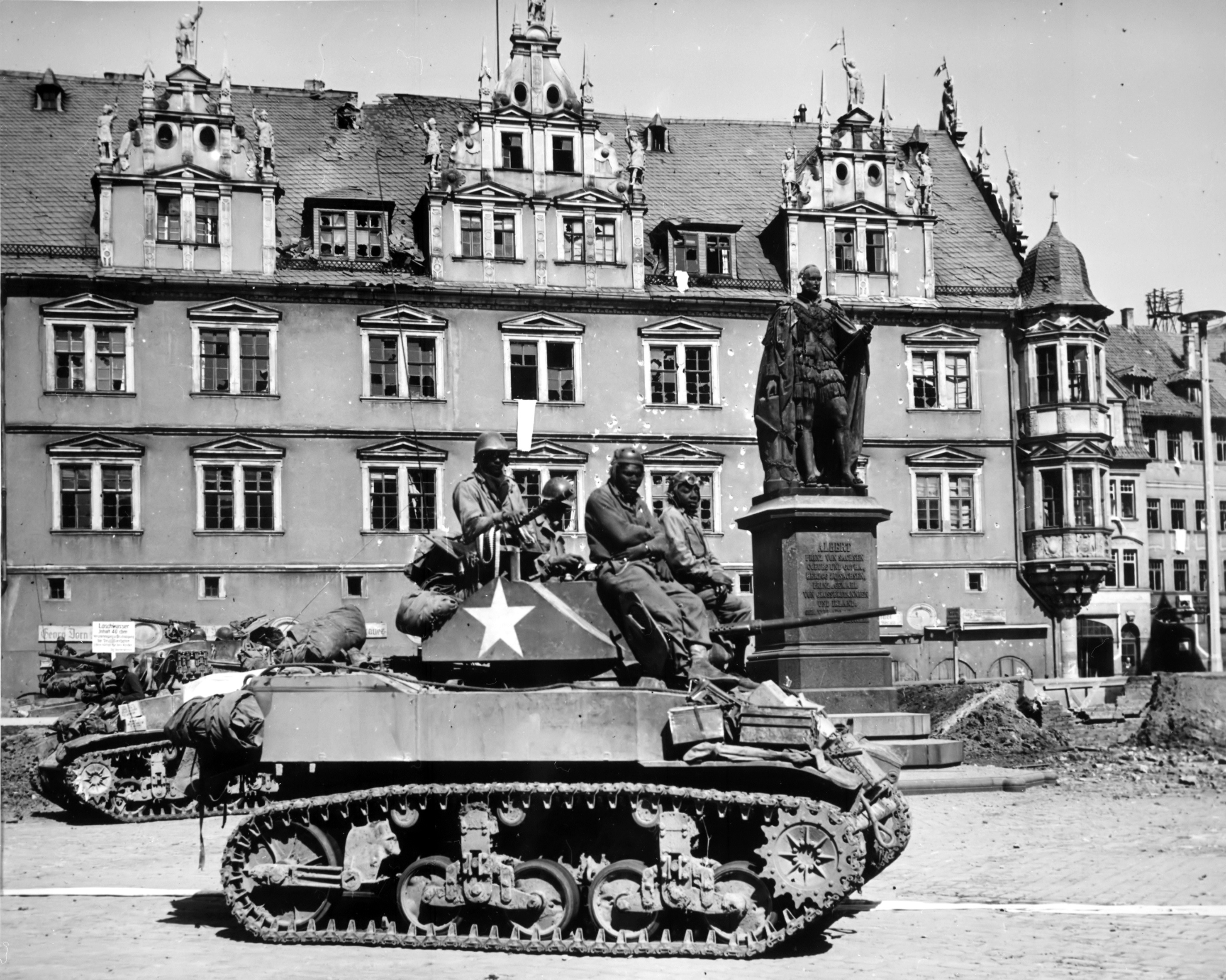 US Army African-American crew of the 761st Tank Battalion on a M5A1 Stuart light tank in Coburg, Bayreuth, Germany, 25 Apr 1945. Note white flags hanging from upper palace windows. Also note evidence that those windows have been machine gunned.