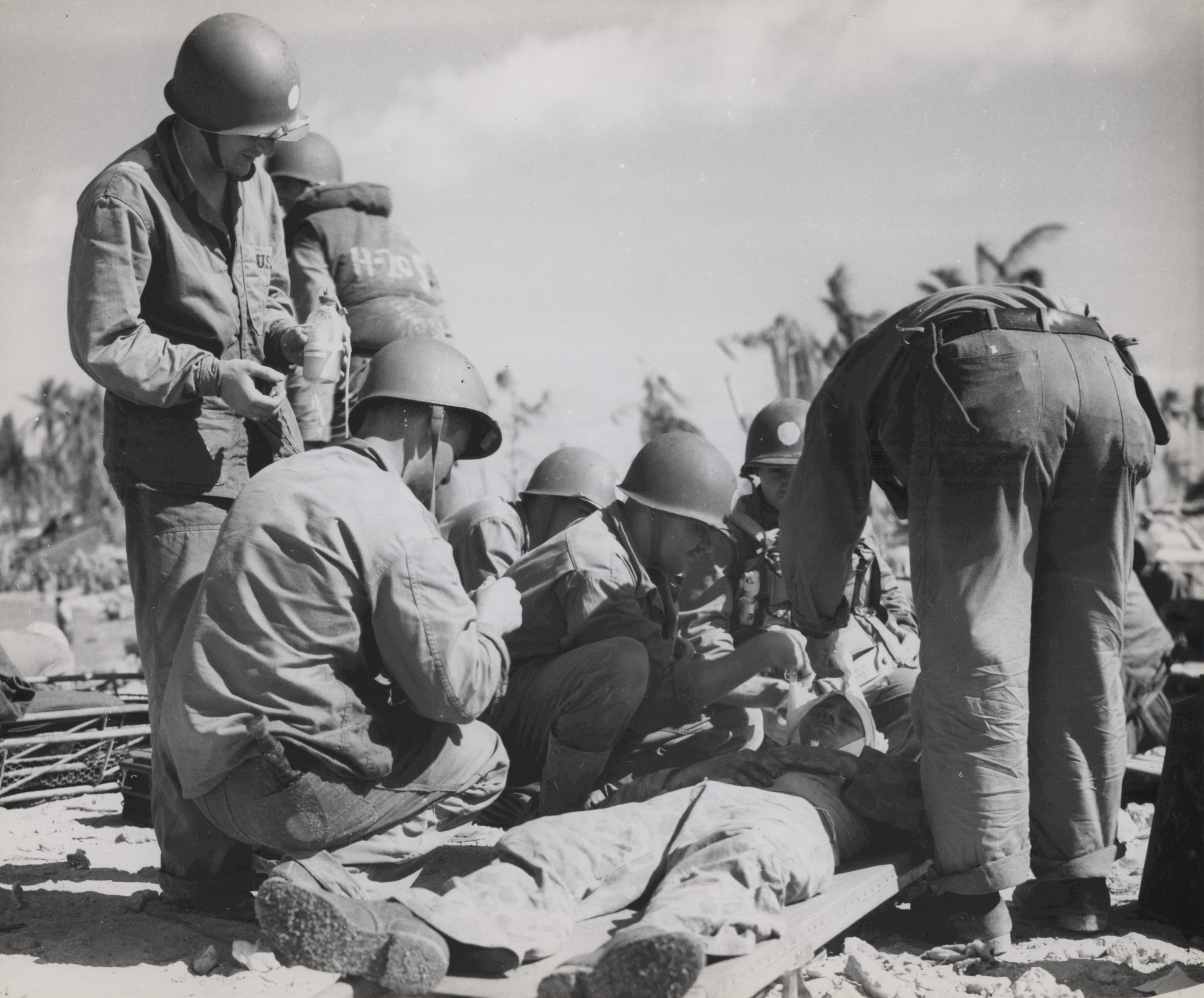 US Navy doctor bandaging a head wound for a US Marine, Tarawa, Gilbert Islands, Nov 1943; note the Marine standing on left held a flask of blood plasma
