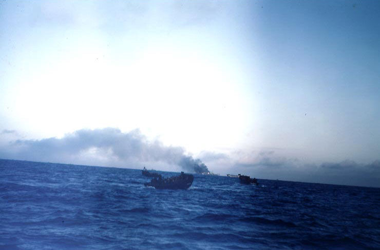 A LCVP loaded with troops sailed on foreground while American ships beyond burned, off Iwo Jima, Feb 1945