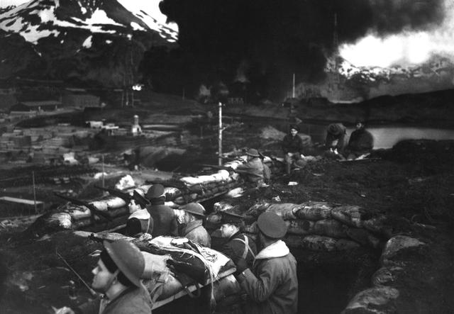 US Marines in a trench at Dutch Harbor, US Territory of Alaska, 3 Jun 1942; note burning fuel tanks in background