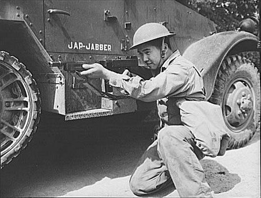 An ethnically Chinese soldier of the US Army posing with a Thompson sub-machinegun next to a halftrac armored car, Fort Knox, Kentucky, United States, Jun 1942