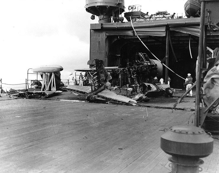 Damage to hangar doors of seaplane tender USS Curtiss by Japanese 250kg bomb during Pearl Harbor attack, 7 Dec 1941, photo 2 of 2; note wreckage of OS2U-2 floatplane in foreground