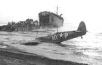 Supermarine Spitfire of the US 307th Fighter Squadron rests on the beach at Paestum, Italy near Salerno after being shot down Sep 9, 1943; pilot uninjured. LST-391 unloads men and materiel beyond, Sep 1943. Photo 1 of 2
