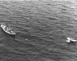 OS2U Kingfisher floats on the ocean near a US Coast Guard cutter as they rescue survivors of a merchant ship torpedoed off the US East Coast; photograph from a US Navy airship, 1942