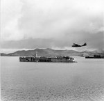 A PBY Catalina flying past the Escort Carrier USS Sangamon at anchor in the Solomons, 1943.
