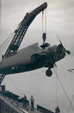 A damaged FM-2 Wildcat being hoisted by a crane from the training aircraft carrier USS Sable to a waiting barge on Lake Michigan, United States, 1943-45.