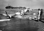 Supermarine Spitfire of the US 307th Fighter Squadron rests on the beach at Paestum, Italy near Salerno after being shot down Sep 9, 1943; pilot uninjured. LST-359 unloads men and materiel beyond, Sep 1943. Photo 2 of 2