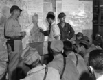 US Army Ground Liaison Officer Maj Mortimer Jordan, left, Japanese POW 2Lt Minoru Wada, center, and interpreter Sgt Charles Imai provide a briefing for fighter and bomber pilots of the 1st Marine Air Wing, Aug 9, 1945