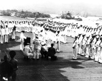 Admiral Chester Nimitz aboard USS Enterprise to present awards, Pearl Harbor, Territory of Hawaii, 27 May 1942. Note capsized USS Oklahoma and sunken USS West Virginia and USS Arizona in the background.