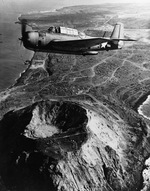 TBM-3 Avenger flying over Mt Suribachi on Iwo Jima after US forces had fully occupied the island, Mar-Apr 1945. Note storage tanks, tents, and other improvements set up by US forces.