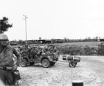 A Jeep full of US 101st Airborne paratroopers at a Normandy check-point, Jun 1944. Note Horsa gliders in the background and a box of full M1 Garand ammunition clips in the immediate foreground behind the MP’s leg.