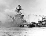 USS Nevada aground and burning off Waipio Point, Pearl Harbor, Hawaii after the Japanese attack, 7 Dec 1941. At right are the harbor tug USS Hoga and minesweeper USS Avocet