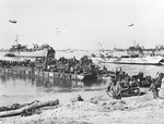 Rhino ferry RHF-19 landing CCKW trucks and other vehicles on Omaha Beach, circa 10 Jun 1944. Note Soldier in the right foreground, with waterproofing taped around his rifle.