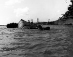The overturned battleship USS Oklahoma, sunk by torpedoes in the Japanese air attack on Pearl Harbor, Hawaii, 7 Dec 1941. Maryland is at right and California’s masts and Ford Island water tower are in the distance.