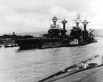 Battleships USS Tennessee (left, floating) and USS West Virginia (right, sunk) at Pearl Harbor’s Battleship Row, 10 Dec 1941. The masts of the sunken USS Arizona can be seen behind the West Virginia.