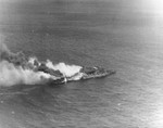 Aerial view of the USS Santa Fe close aboard the badly burning USS Franklin, 19 Mar 1945, southeast of Japan. Note Franklin’s buckled forward elevator and the water streams from Santa Fe’s stern onto the Franklin.